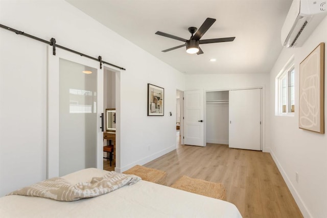 bedroom featuring ceiling fan, a barn door, an AC wall unit, light hardwood / wood-style flooring, and a closet