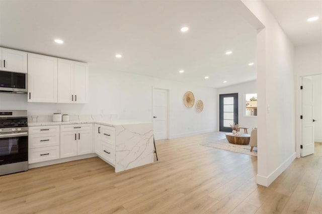 kitchen featuring white cabinetry, stainless steel appliances, vaulted ceiling, light hardwood / wood-style flooring, and light stone counters