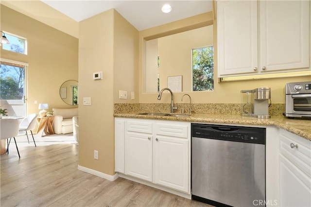 kitchen with stainless steel dishwasher, sink, white cabinetry, light wood-type flooring, and light stone countertops