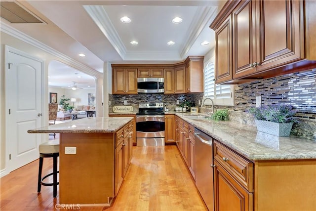 kitchen with a kitchen island, stainless steel appliances, sink, ceiling fan, and a breakfast bar