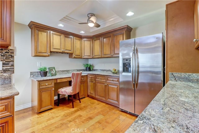 kitchen with light stone counters, stainless steel fridge with ice dispenser, a raised ceiling, and light wood-type flooring