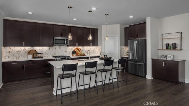 kitchen featuring appliances with stainless steel finishes, dark hardwood / wood-style floors, tasteful backsplash, a kitchen island with sink, and pendant lighting