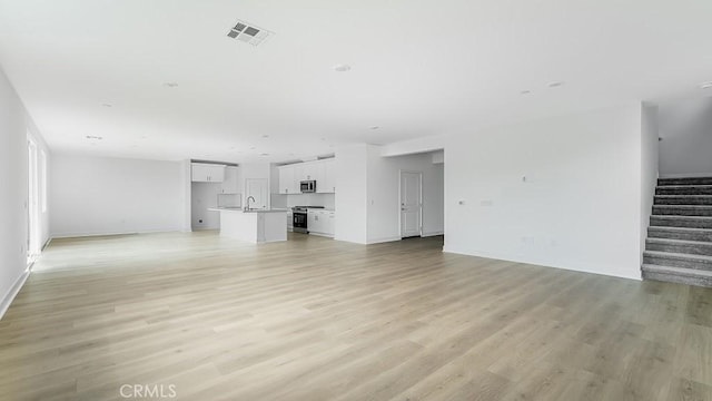 unfurnished living room featuring stairway, baseboards, visible vents, light wood finished floors, and a sink