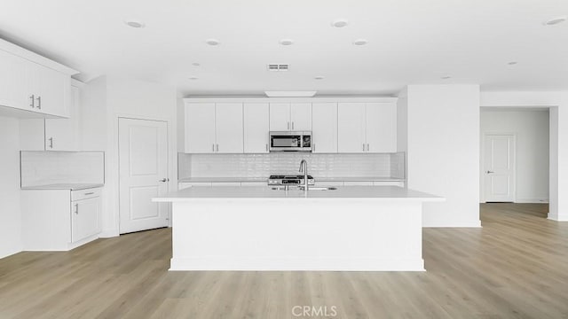 kitchen with stainless steel microwave, light countertops, a center island with sink, and light wood finished floors