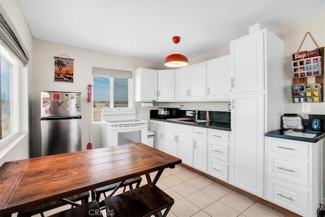 kitchen with stainless steel fridge, a wealth of natural light, white cabinets, white range with electric cooktop, and sink