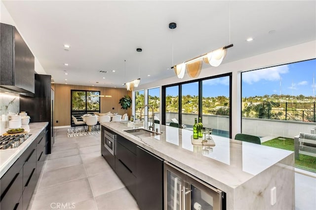 kitchen featuring decorative light fixtures, a large island with sink, wood walls, sink, and beverage cooler