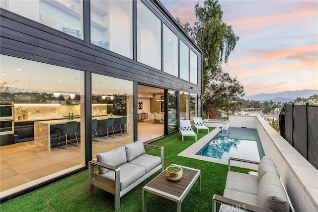 pool at dusk with a mountain view, outdoor lounge area, a yard, and a patio