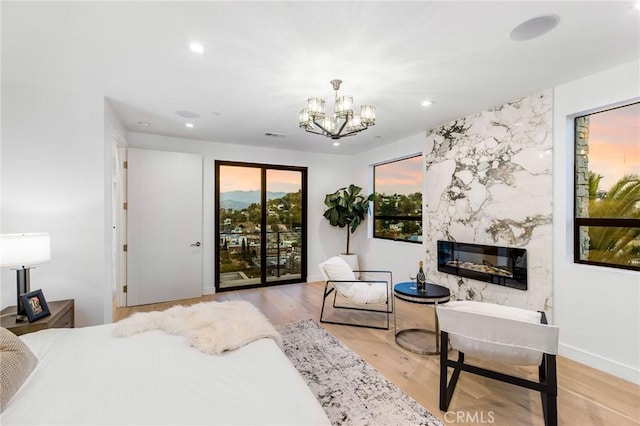 bedroom with a high end fireplace, access to outside, a notable chandelier, and light wood-type flooring