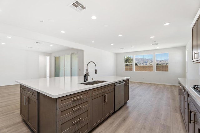 kitchen with an island with sink, dishwasher, light hardwood / wood-style floors, and sink