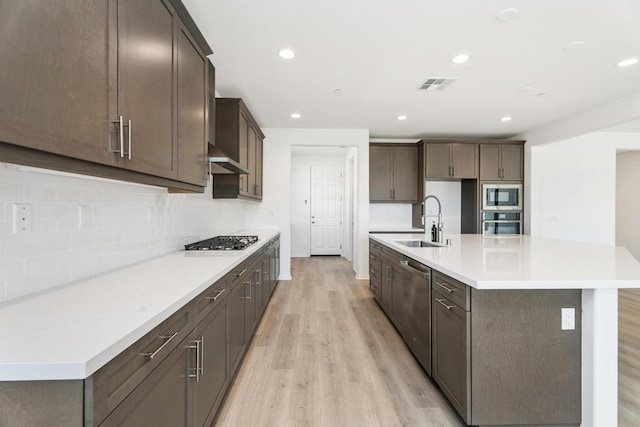 kitchen featuring appliances with stainless steel finishes, tasteful backsplash, sink, a kitchen island with sink, and light hardwood / wood-style flooring