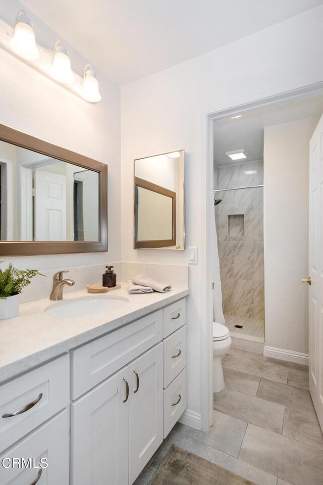 bathroom with toilet, tiled shower, and vanity