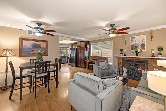 living room with a brick fireplace, ornamental molding, light hardwood / wood-style floors, and ceiling fan