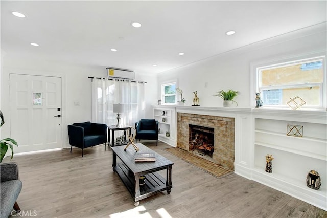 living room with built in features, crown molding, a wall mounted AC, and light wood-type flooring