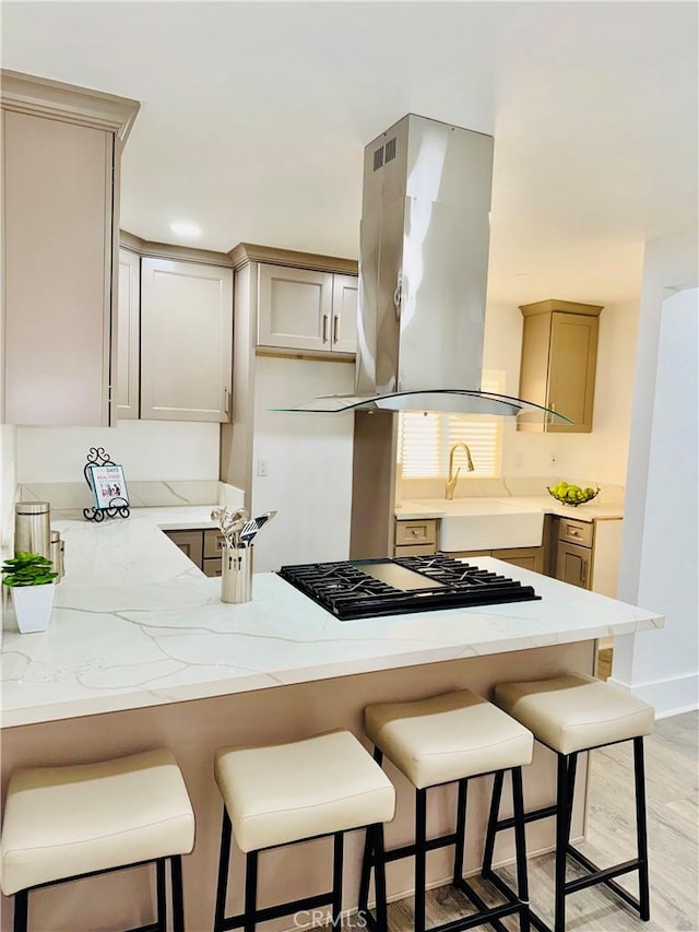 kitchen with island exhaust hood, kitchen peninsula, stainless steel gas cooktop, light hardwood / wood-style flooring, and a breakfast bar area