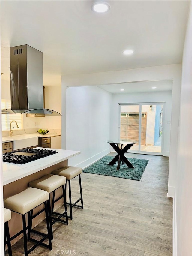 kitchen with gray cabinets, a breakfast bar, gas cooktop, light wood-type flooring, and ventilation hood