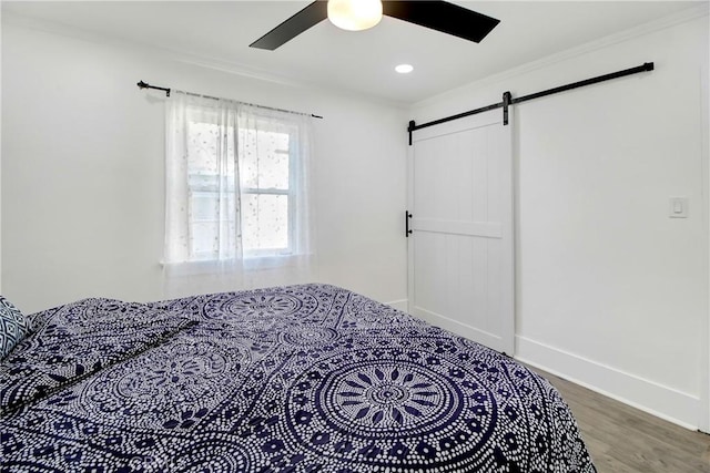 bedroom with ceiling fan, ornamental molding, a barn door, and hardwood / wood-style floors