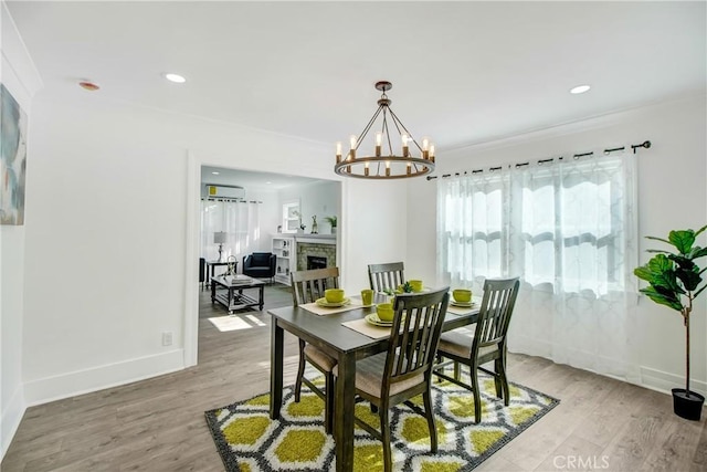 dining space featuring hardwood / wood-style floors, a wall unit AC, a fireplace, ornamental molding, and a chandelier