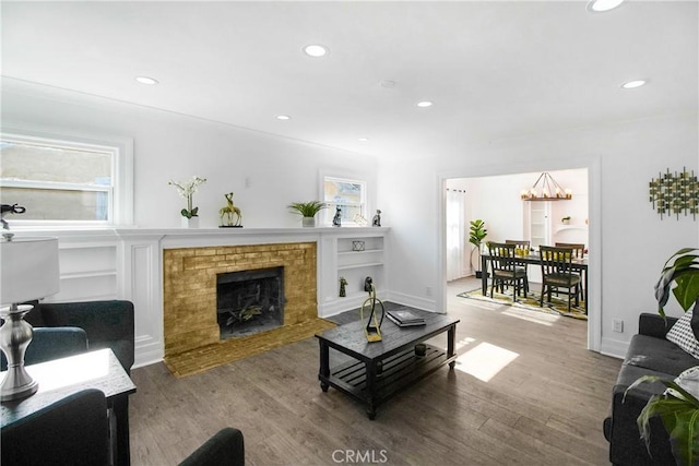 living room featuring a brick fireplace, a chandelier, hardwood / wood-style flooring, and built in shelves