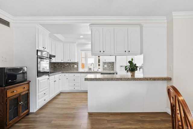 kitchen featuring kitchen peninsula, backsplash, crown molding, white cabinets, and black appliances