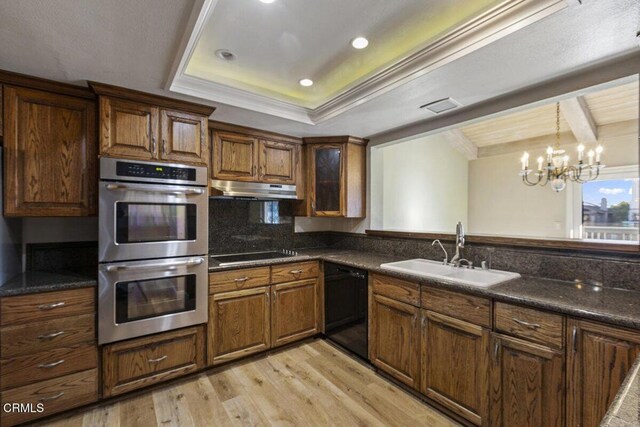 kitchen featuring a raised ceiling, a notable chandelier, dishwasher, double oven, and sink