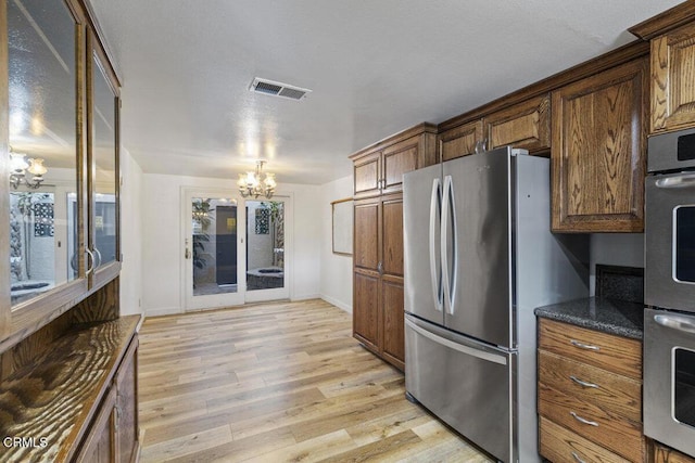 kitchen featuring a notable chandelier, dark stone counters, stainless steel appliances, and light hardwood / wood-style floors