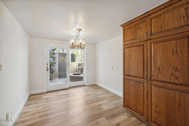 unfurnished dining area with a notable chandelier, light wood-type flooring, and baseboards