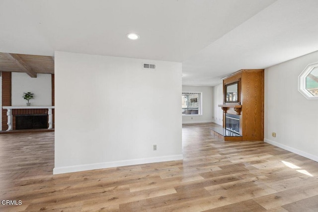 unfurnished living room with visible vents, baseboards, light wood-type flooring, and a brick fireplace