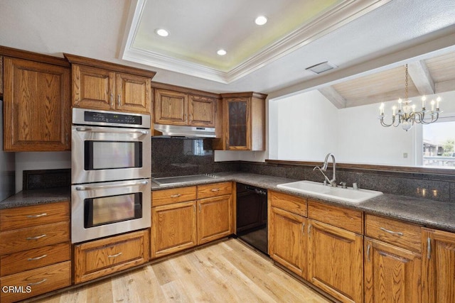 kitchen featuring dark countertops, black appliances, under cabinet range hood, brown cabinetry, and a sink