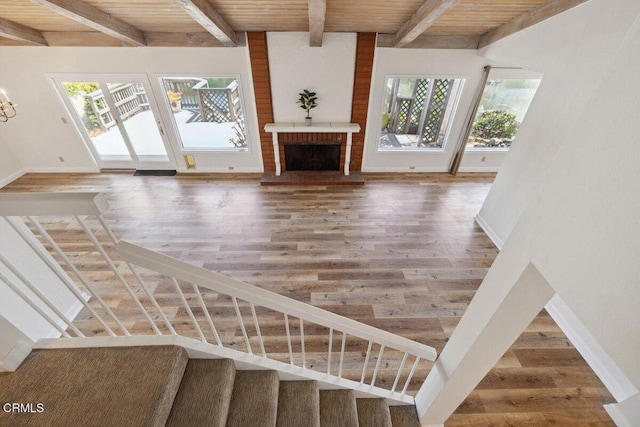 unfurnished living room with stairway, baseboards, beam ceiling, and wood finished floors