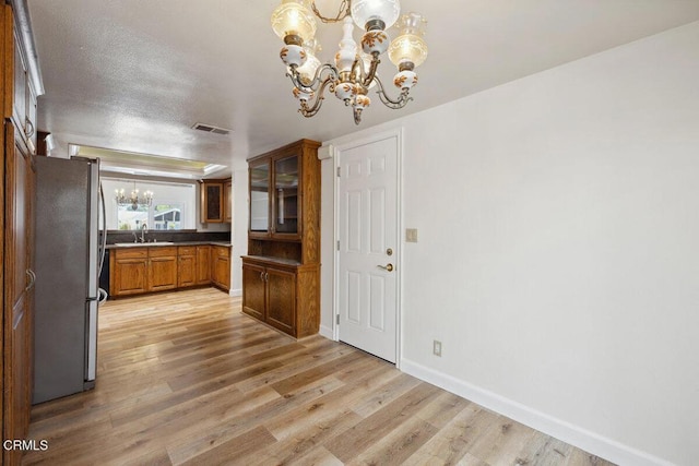 kitchen with visible vents, an inviting chandelier, freestanding refrigerator, brown cabinetry, and light wood finished floors