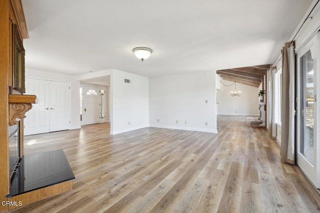 unfurnished living room featuring visible vents, light wood-style flooring, a notable chandelier, and baseboards
