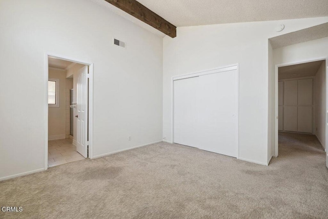 unfurnished bedroom featuring carpet, a closet, visible vents, vaulted ceiling with beams, and baseboards