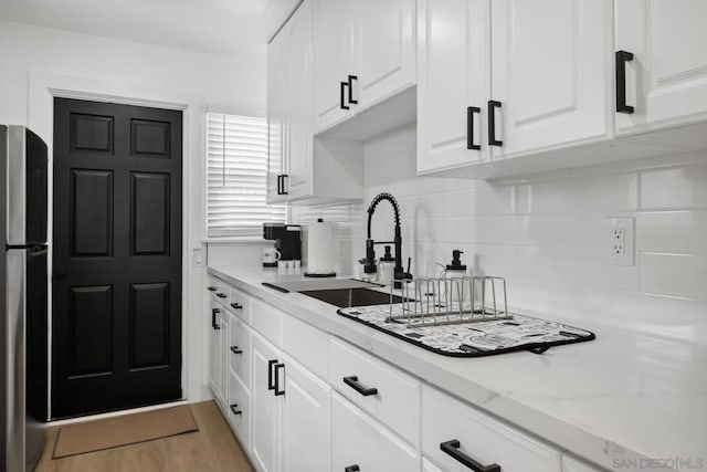 kitchen with stainless steel fridge, backsplash, light stone countertops, white cabinets, and sink