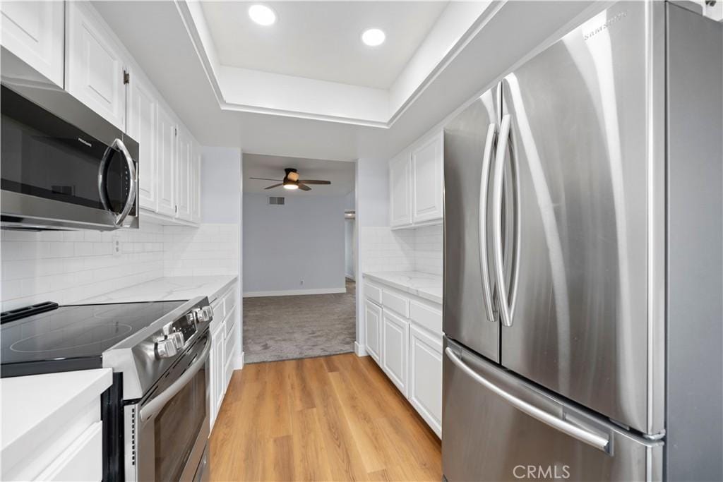 kitchen featuring white cabinets, light wood-type flooring, light stone countertops, and stainless steel appliances