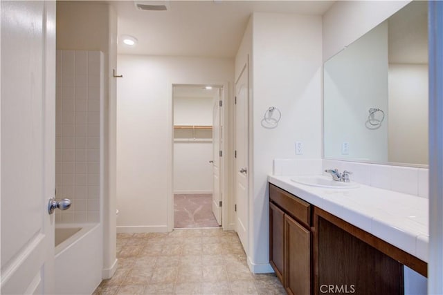 bathroom with visible vents, baseboards, a walk in closet, and vanity