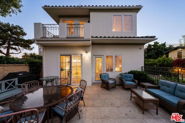 back house at dusk with a patio area, outdoor lounge area, and a balcony