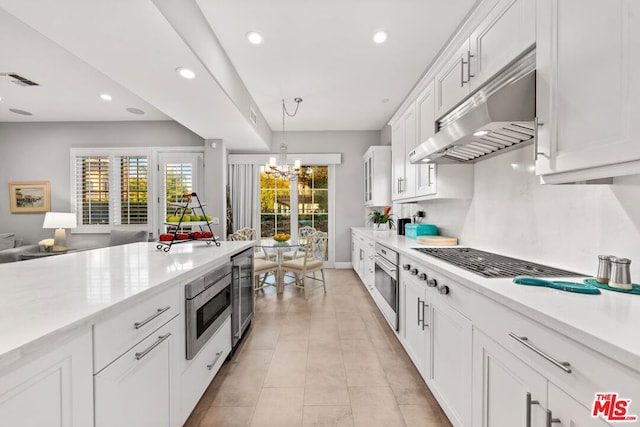 kitchen with an inviting chandelier, white cabinetry, hanging light fixtures, stainless steel oven, and beverage cooler