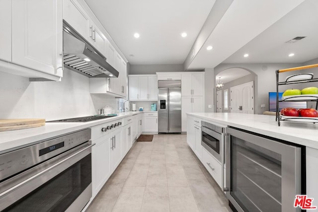 kitchen with beverage cooler, white cabinetry, built in appliances, an inviting chandelier, and sink