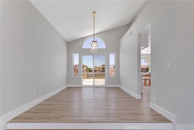 unfurnished dining area with high vaulted ceiling, light hardwood / wood-style flooring, and a notable chandelier