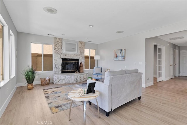 living room with a wealth of natural light, a stone fireplace, and light hardwood / wood-style floors