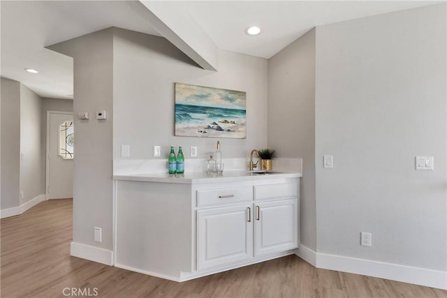 bar with sink, white cabinets, and light hardwood / wood-style flooring