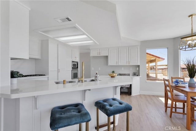 kitchen featuring decorative light fixtures, kitchen peninsula, a kitchen bar, appliances with stainless steel finishes, and white cabinets