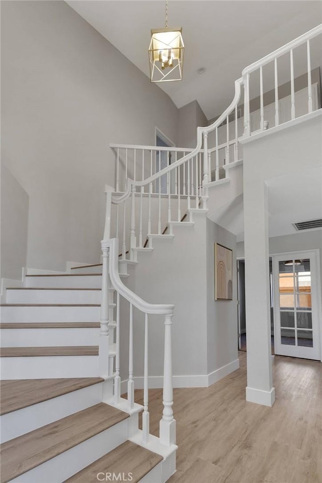 stairs with vaulted ceiling, an inviting chandelier, and hardwood / wood-style flooring