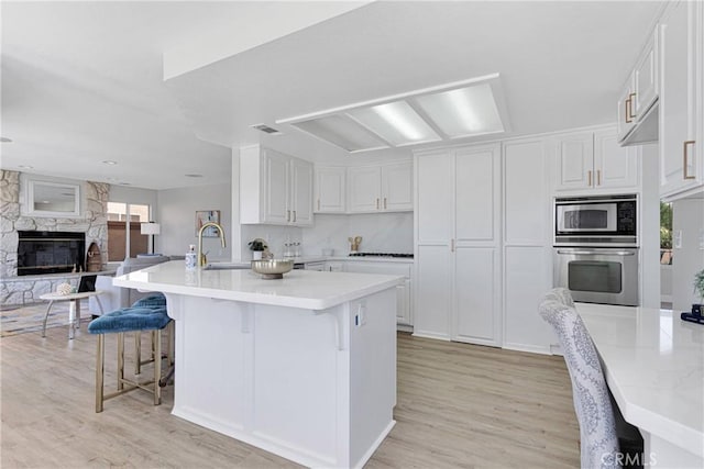 kitchen with white cabinets, a fireplace, stainless steel oven, a breakfast bar area, and built in microwave