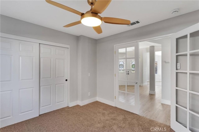 unfurnished bedroom featuring ceiling fan, light colored carpet, a closet, and french doors