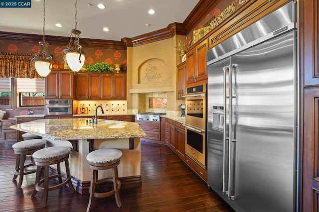 kitchen with decorative light fixtures, sink, appliances with stainless steel finishes, an island with sink, and light stone counters