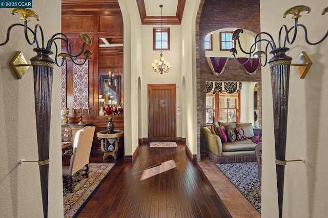 foyer entrance featuring dark hardwood / wood-style flooring, ornamental molding, a towering ceiling, and an inviting chandelier