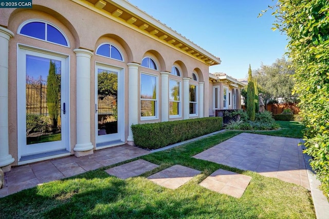 view of exterior entry with a lawn and a patio area