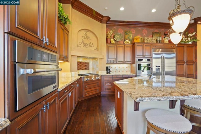 kitchen with decorative light fixtures, a kitchen breakfast bar, appliances with stainless steel finishes, and a center island with sink