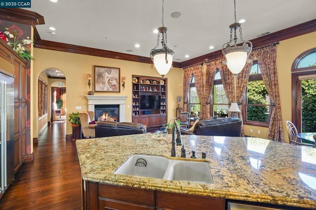 kitchen with decorative light fixtures, light stone countertops, sink, and a center island with sink